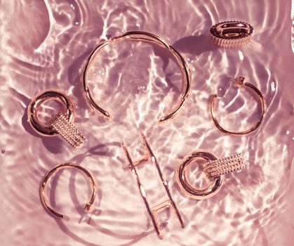 Rose gold bracelets, earrings, rings, jewelery on pink water background, luxury glamour and holiday beauty design for jewelry brand ads