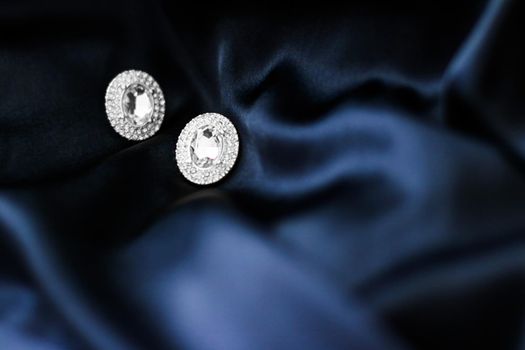 Luxury diamond earrings on dark blue silk background, holiday glamour jewelery present