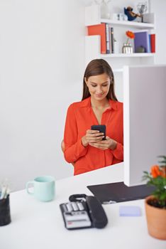Taking a moment to stay connected. A young woman at the office while using her phone.