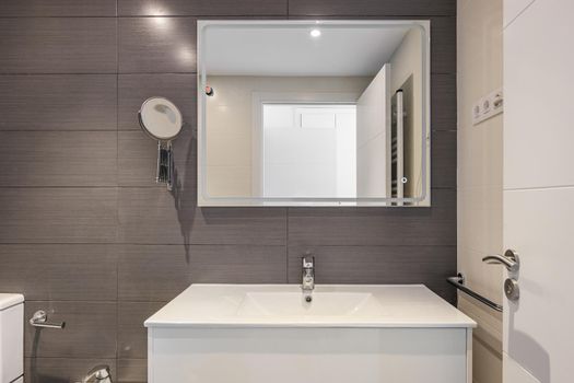 Modern bathroom with gray tiles, toilet and rectangular large mirror with lighting