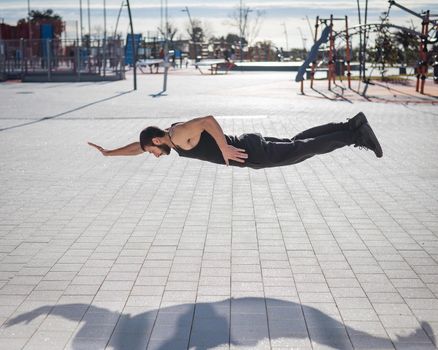 A man in black sportswear jumps doing push-ups in the park.