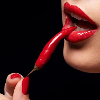 The other forbidden fruit. Closeup of a woman holding a red chilli to her mouth.