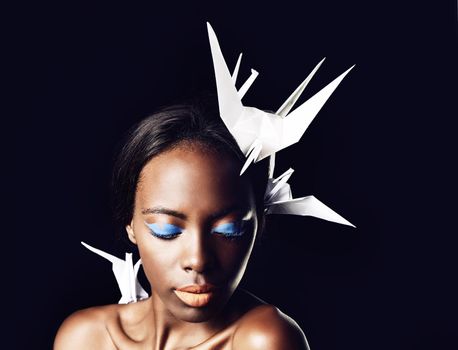 She symbolizes African beauty. a beautiful ethnic woman posing with origami birds on her head and shoulders.