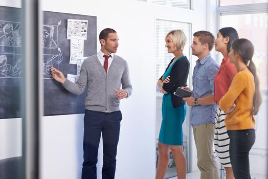 Hes a leader they can look up to. A businessman standing and presenting a storyboard to his team in an office.