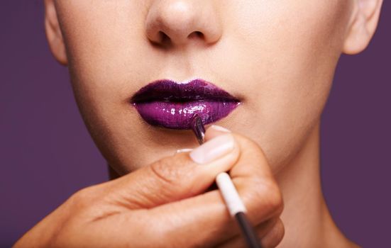 Shes a vision in violet. a woman having purple lipstick applied to her lips.