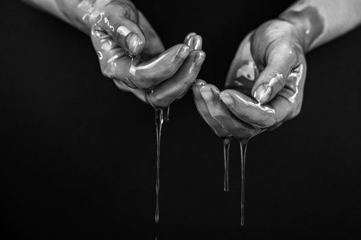 Women's hands in a viscous liquid similar to blood. Black and white photo.