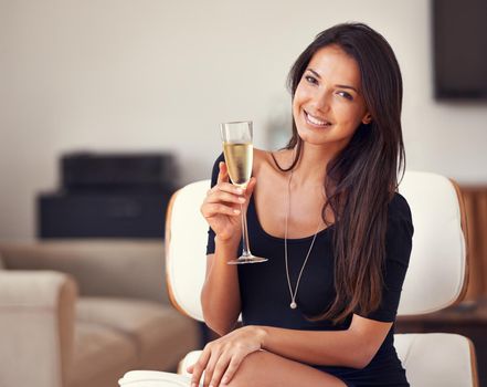 Heres to health, wealth and happiness. A cropped portrait of a beautiful young woman sitting in a living room with a glass of champagne.