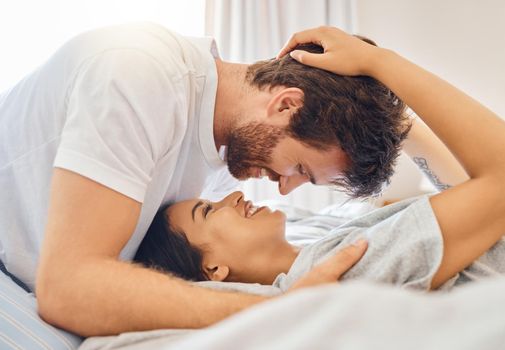Couple, love and happy with a man and woman in bed in the bedroom of their home together with a smile. Romance, dating and affection with a young male and female bonding and being intimate in a house