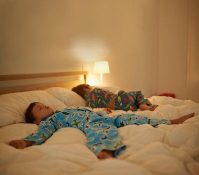 Sleepovers are the best. two little boys sleeping on a bed with the light on.