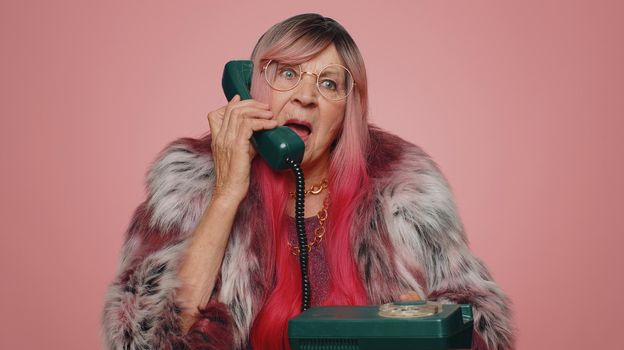 Crazy hotline agent old woman talking on wired vintage telephone of 80s fooling making silly faces