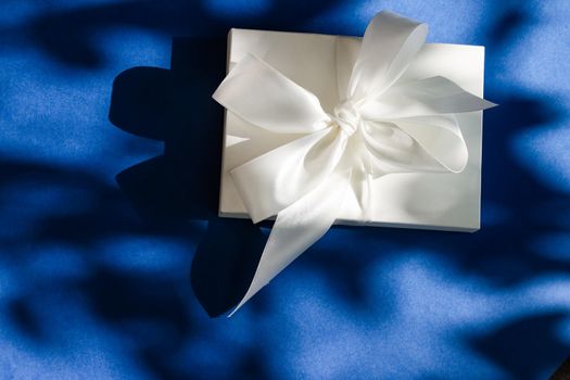 Luxury holiday white gift box with silk ribbon and bow on blue background, luxe wedding or birthday present