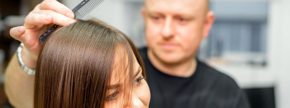 Young caucasian brunette woman having her hairstyling by a male hairdresser at a parlor.