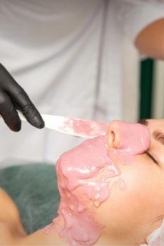 The cosmetologist applying an alginate mask to the face of a young woman in a beauty salon.