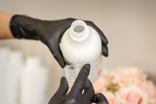 A hairdresser in black gloves is preparing hair dye with a bottle in a hair salon, close up.