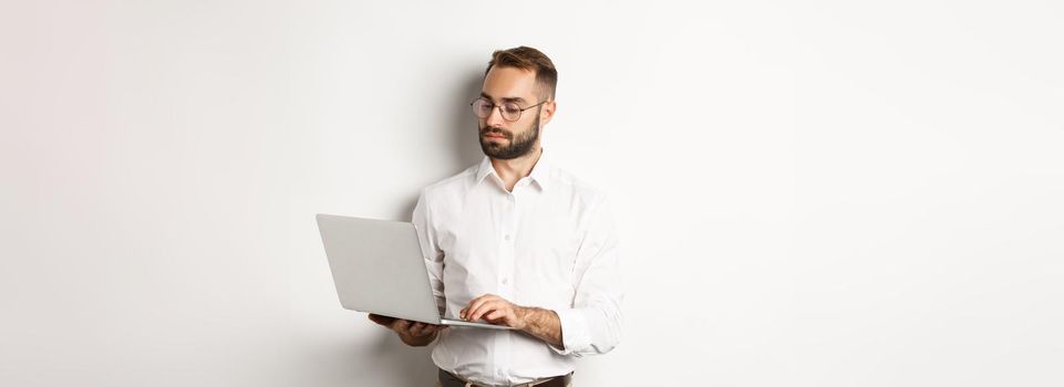 Business. Serious manager working on laptop, standing over white background