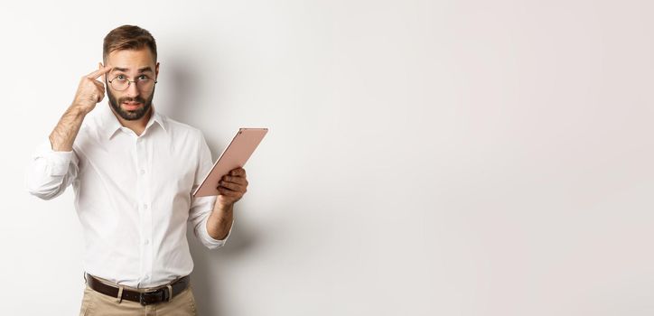 Displeased employer scolding staff while checking report on digital tablet, pointing at head and looking disappointed, standing over white background