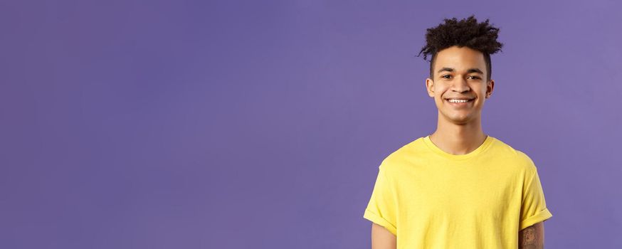 Close-up portrait of nice, friendly-looking hispanic male student in yellow t-shirt, grinning delighted, look upbeat happy and positive, standing enthusiastic with beaming smile purple background