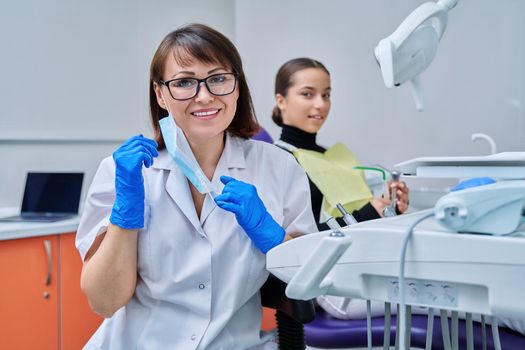Portrait of female dentist looking at camera with young teen girl patient sitting in dental chair. Dentistry, hygiene, treatment, dental health care concept