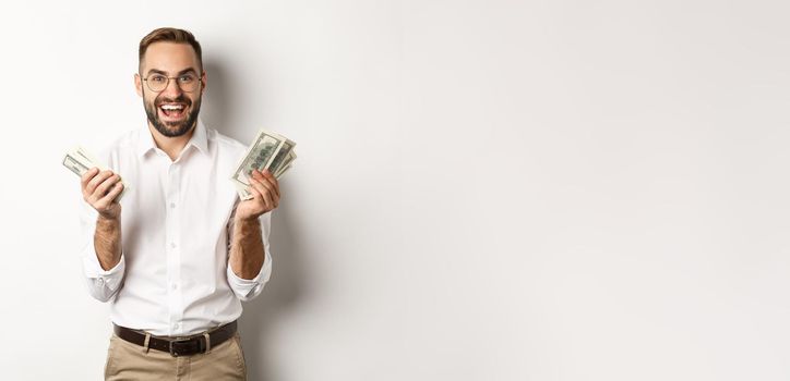 Handsome successful business man counting money, rejoicing and smiling, standing over white background