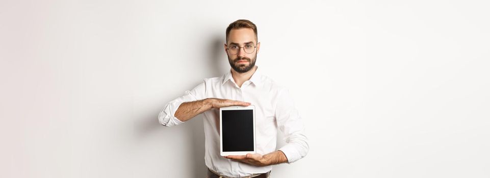 Confident bearded man showing digital tablet screen, demonstrating app, standing over white background