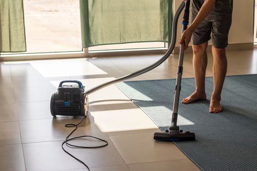 Shot of man vacuuming the carpet i the room. Chores
