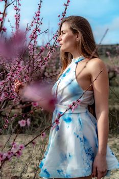 Young beautiful woman in blue dress and long hair is enjoying with blossoming peach trees