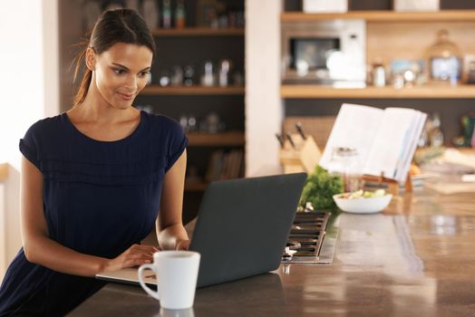 A good kitchen is a focal point of the home. an attractive young woman using her laptop while enjoying a cup of coffee.