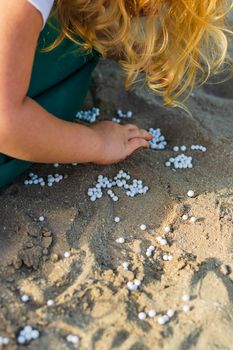 Close up shot of a little girl's hand playing with styrofoam from bean bag on the sand . Outdoors