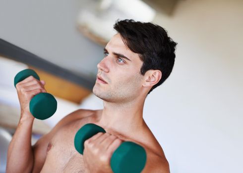 Focus and determination. A cropped shot of a focused young man lifting dumbbells at home.