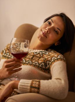 Relaxing with a glass of fine wine. an attractive young woman enjoying a glass of wine while relaxing at home.