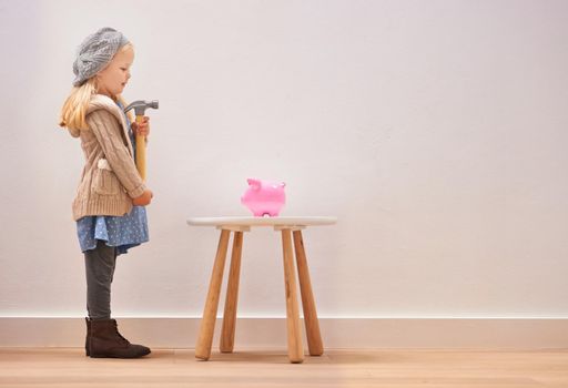 To break or not to break. A little girl standing in front of her piggy bank with a hammer.