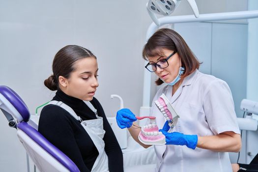 Teenage female sitting in dental chair, doctor with jaw model and toothbrush