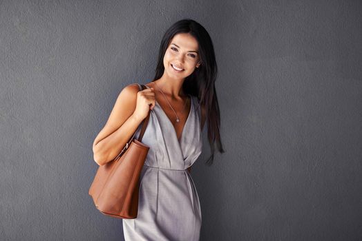 Shes packing a purse and a smile. Studio portrait of an attractive young woman holding her handbag.