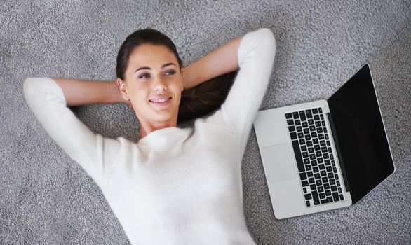 So easy it almost works itself. a young woman lying on a rug next to a laptop.