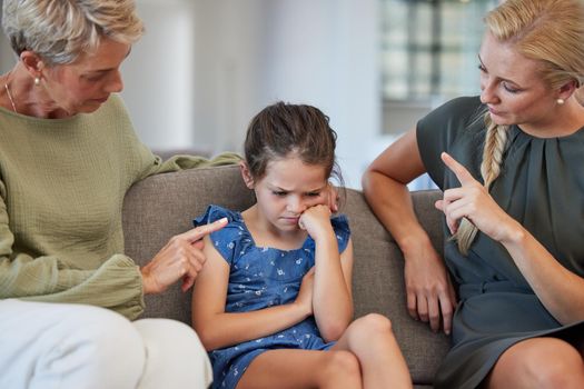 Family, discipline and warning by mother and grandmother hand sign to girl for bad behaviour on a sofa at home. Autism, adhd and communication by parent and daughter in conflict with attitude problem