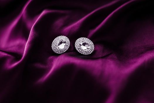 Luxury diamond earrings on dark pink silk fabric, holiday glamour jewelery present