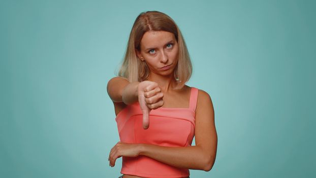 Upset woman in casual crop top showing thumbs down sign gesture, disapproval, dissatisfied dislike