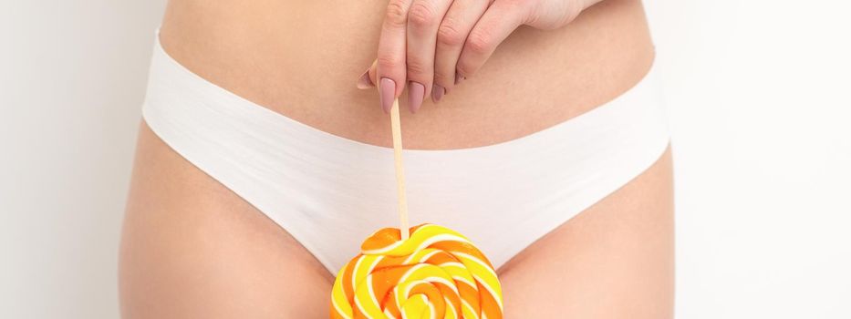 Hand of a woman wearing white panties holding lollipop on a stick covering the intimate area, the concept of intimate depilation, problems of intimate hygiene.