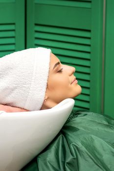 Hairdresser wraps hair of a young caucasian woman in a white towel after washing head in the hairdressing salon.