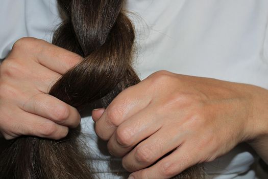 A girl with long dark hair is braiding her hair. Close-up hands. Hair care. Hair loss problem
