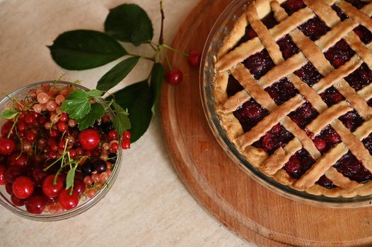 Top view of classic American festive cherry pie with crispy sweet pastry lattice and fresh ripe organic berries in bowl