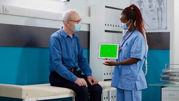 Nurse showing tablet with greenscreen display to senior man