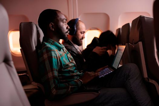 Young businessman travelling in economy class and using laptop