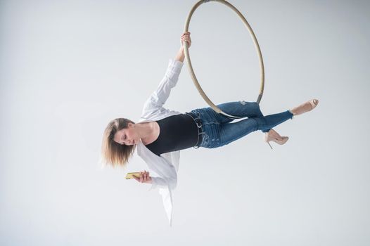 Caucasian female gymnast doing aerial hoop exercises and using smartphone.