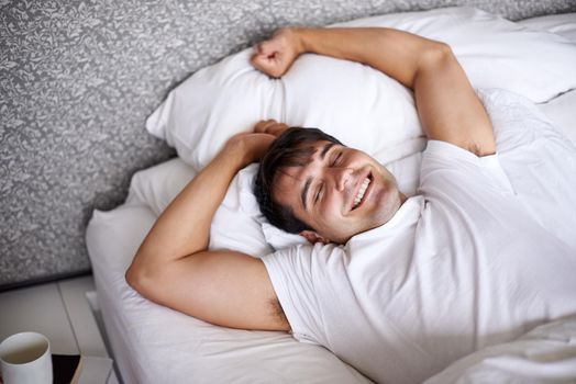 Waking up with a smile. a young man stretching in bed while waking up.