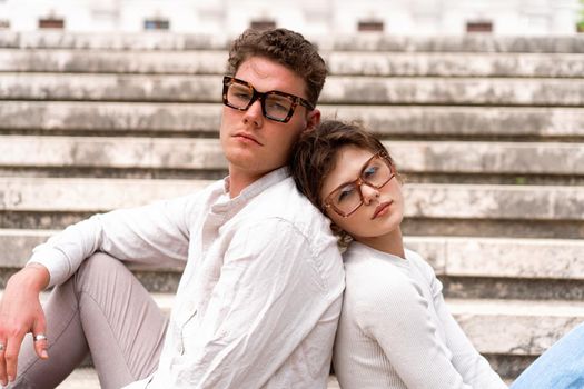 Young beautiful hipster couple in sunglasses in love sitting stairs on old city street