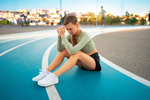 Full length upset sporty woman sitting on running track