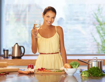 Cheers to good food. A young woman holding a glass of wine while cooking.