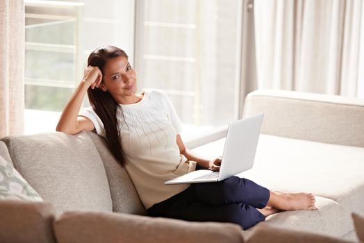 She loves her relaxed weekends. an attractive young woman relaxing on the couch with her laptop.