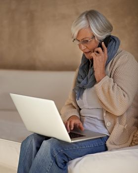 Im checking my emails now...A senior woman on her mobile while using her laptop at home.